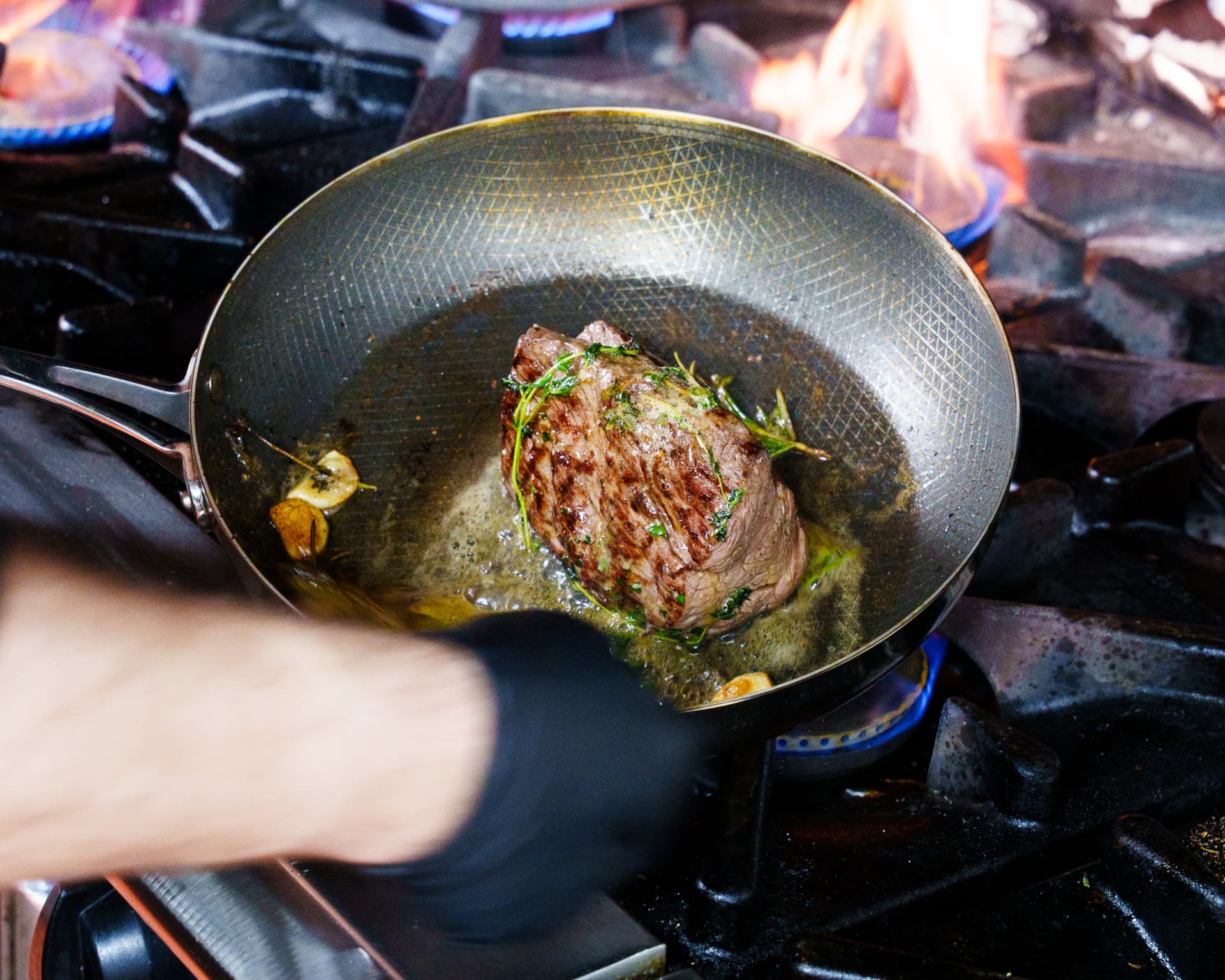 Steak searing in a pan with garlic and herbs
