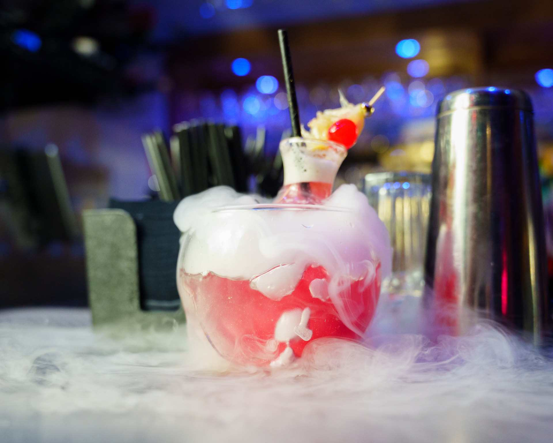 Smoking pink cocktail fishbowl garnished with cherry and pineapple