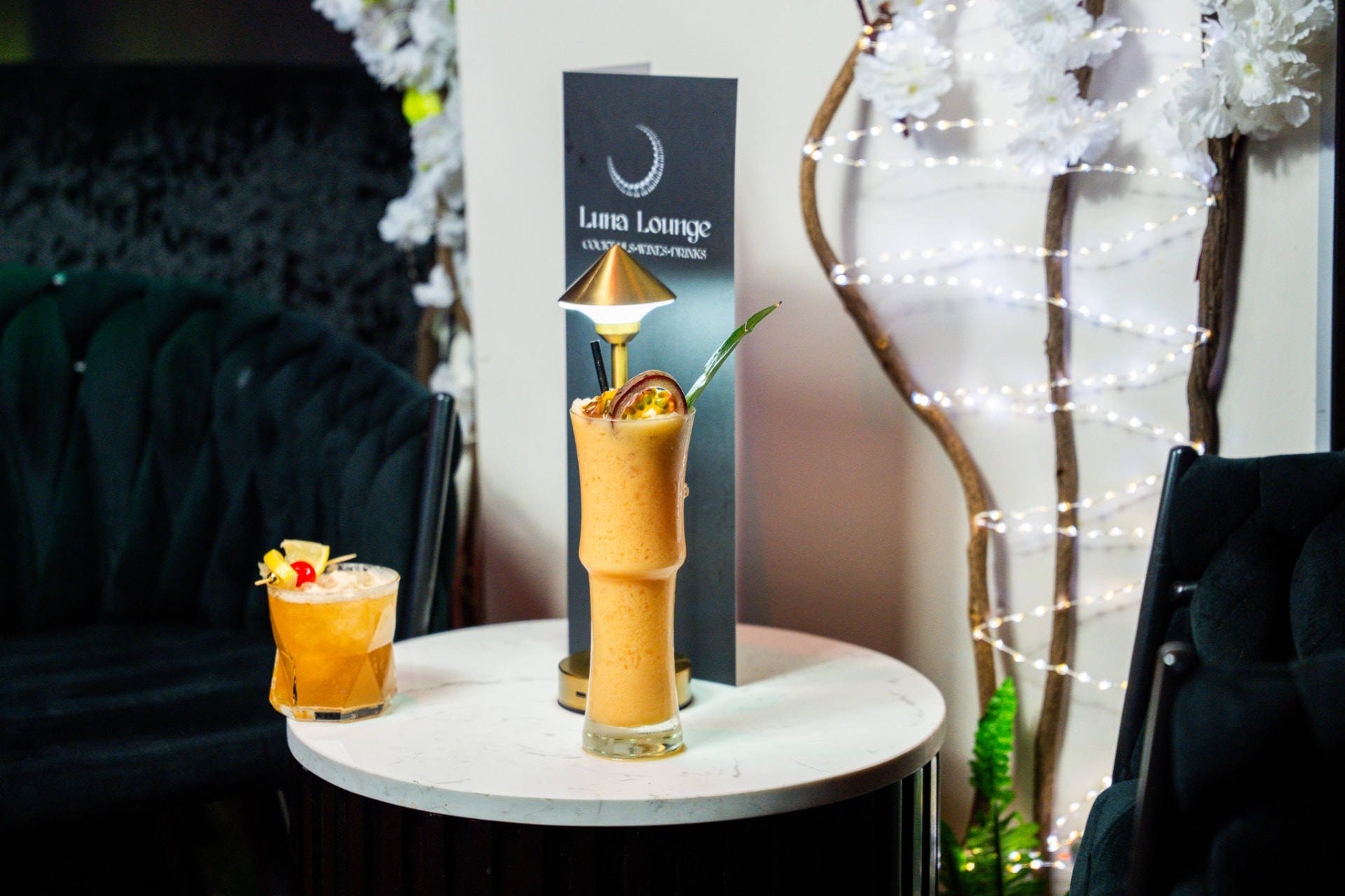 Two cocktails on a table with Luna Lounge menu